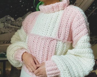Könnte beinhalten: Ein rosa-weißer Häkelpullover mit hohem Kragen und langen Ärmeln. Der Pullover hat ein Patchwork-Design mit Quadraten in verschiedenen Farben.