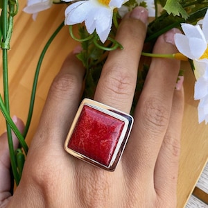 Puede incluir: Un anillo de forma cuadrada con una piedra de coral rojo engastada en un marco de plata.
