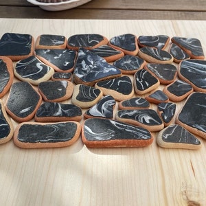 May include: A collection of 20 black and white marbled ceramic tiles with a light brown border. The tiles are arranged in a random pattern on a light wood surface.