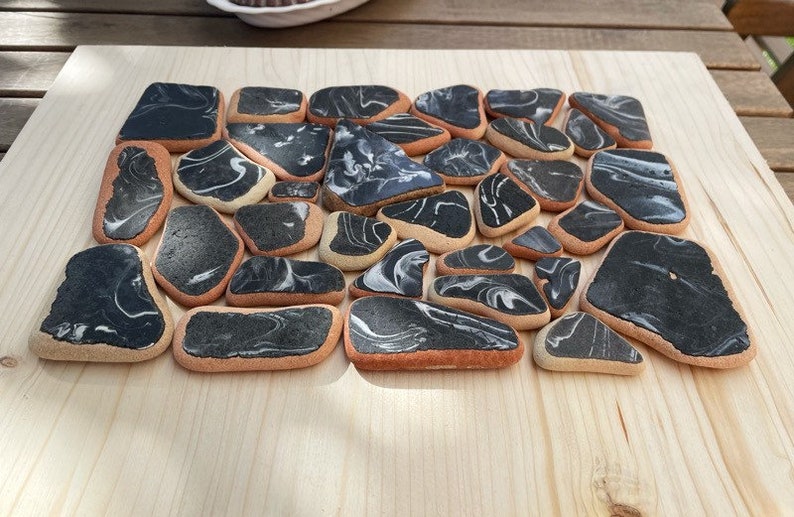 May include: A collection of 20 black and white marbled ceramic tiles with a light brown border. The tiles are arranged in a random pattern on a light wood surface.