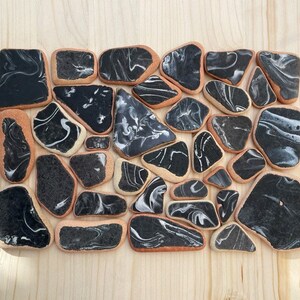 May include: A collection of black and white marbled ceramic tiles arranged in a rectangular shape. The tiles are irregularly shaped and have a smooth, glossy finish.