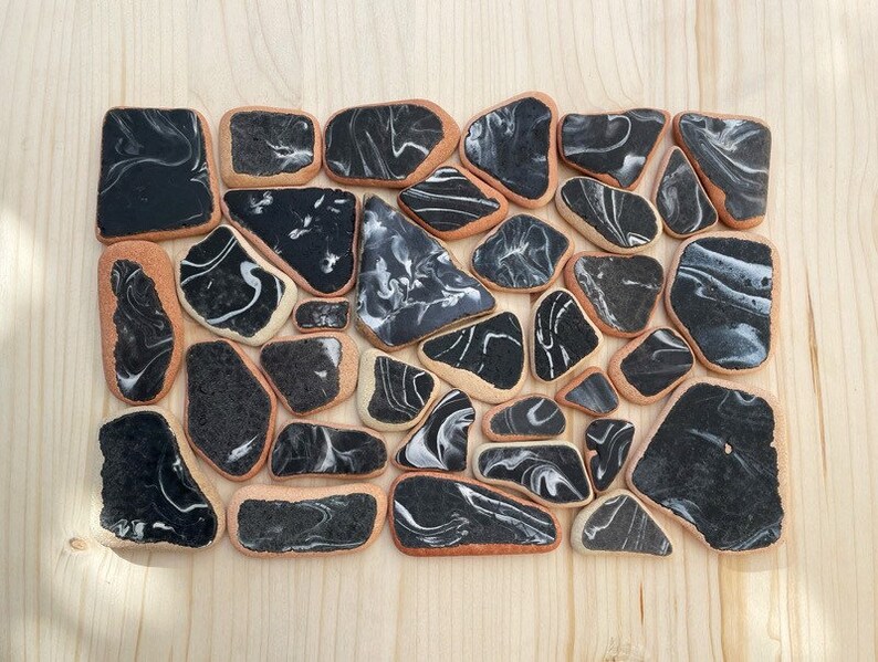May include: A collection of black and white marbled ceramic tiles arranged in a rectangular shape. The tiles are irregularly shaped and have a smooth, glossy finish.