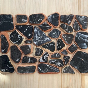 May include: A collection of black and white marbled ceramic tiles arranged in a mosaic pattern. The tiles are irregularly shaped and have a smooth, glossy finish.