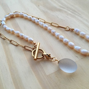 May include: A gold chain necklace with a toggle clasp and a pearl strand. The necklace has a frosted glass pendant.