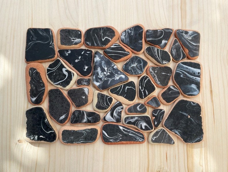 May include: A collection of black and white marbled ceramic tiles arranged in a rectangular shape. The tiles are irregularly shaped and have a smooth, glossy finish.