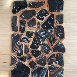 May include: A collection of black and white marbled ceramic tiles with a light brown border. The tiles are arranged in a random pattern and are all different shapes and sizes.
