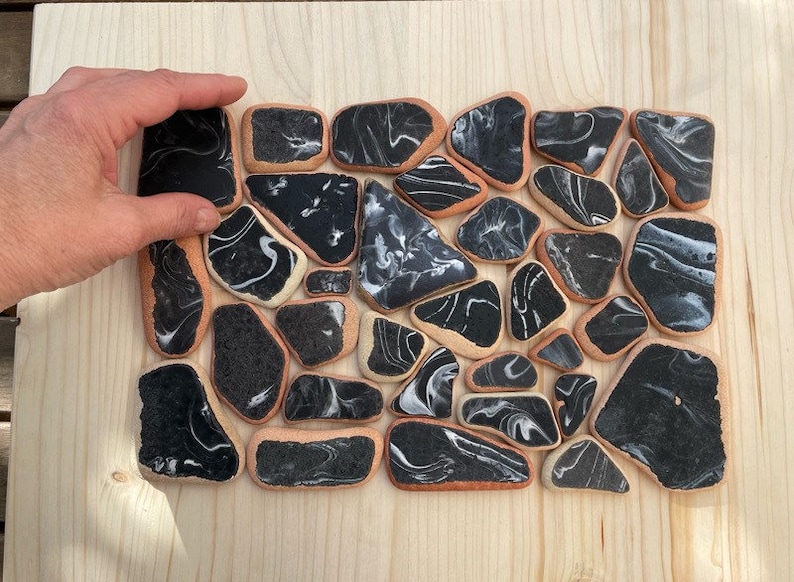 May include: A collection of black and white marbled ceramic tiles arranged in a mosaic pattern. The tiles are irregularly shaped and have a smooth, glossy finish.