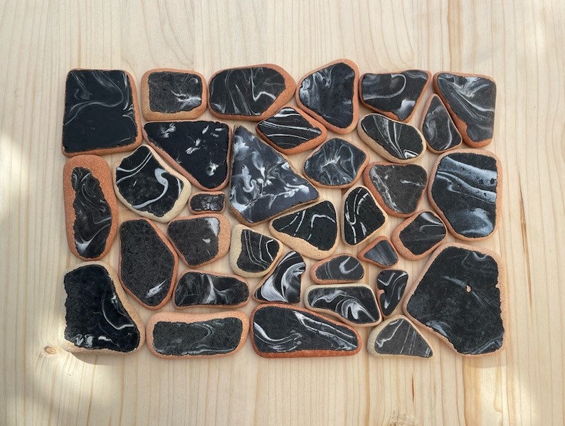 May include: A collection of black and white marbled ceramic tiles arranged in a mosaic pattern. The tiles are irregularly shaped and have a smooth, glossy finish.