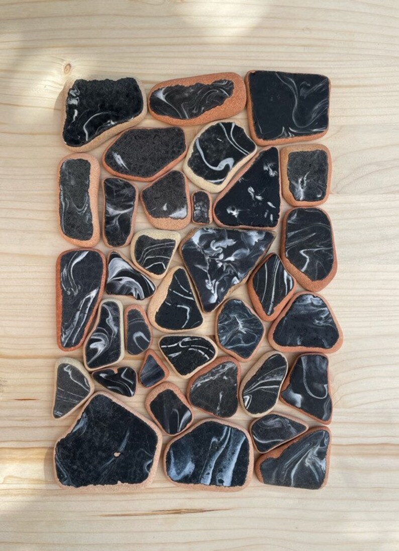 May include: A collection of black and white marbled ceramic tiles with a light brown border. The tiles are arranged in a random pattern and are all different shapes and sizes.