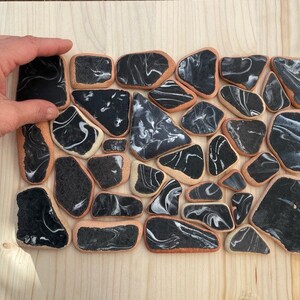 May include: A collection of black and white marbled ceramic tiles arranged in a mosaic pattern. The tiles are irregularly shaped and have a smooth, glossy finish.