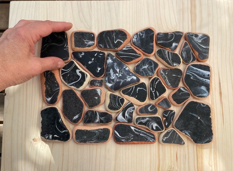 May include: A collection of black and white marbled ceramic tiles arranged in a mosaic pattern. The tiles are irregularly shaped and have a smooth, glossy finish.