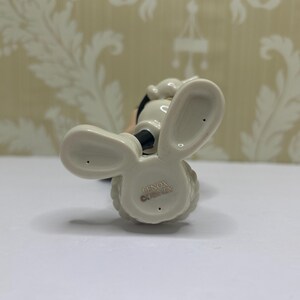 May include: A ceramic figurine of a cartoon character, viewed from below. The figure has large, rounded ears, a black nose, and a white body. The base is marked with "LENOX DISNEY".