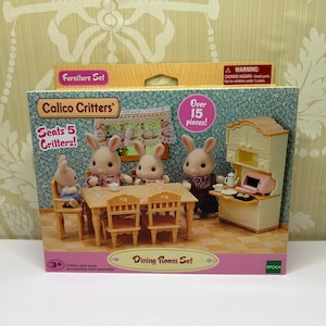 May include: A Calico Critters Dining Room Set box featuring a miniature dining room scene with rabbit figurines. The set includes a table, chairs, a cabinet, and over 15 pieces. The box is pink and green.