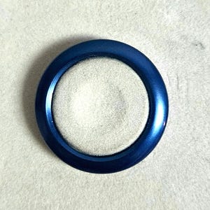 May include: A blue ring with a white center, sitting on a white surface.