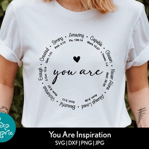 May include: White t-shirt with a black circle design that says "you are" with a heart in the middle. The circle is surrounded by words like "strong", "amazing", "capable", "chosen", "never alone", "always loved", "beautiful", "victorious", "enough", "created". The text at the bottom says "You Are Inspiration SVG | DXF | PNG | JPG".