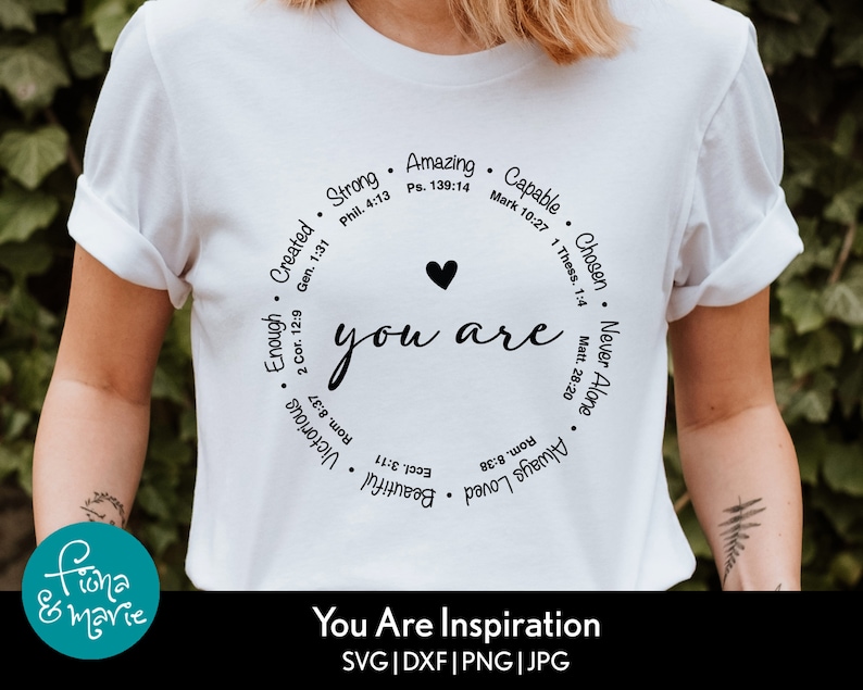May include: White t-shirt with a black circle design that says "you are" with a heart in the middle. The circle is surrounded by words like "strong", "amazing", "capable", "chosen", "never alone", "always loved", "beautiful", "victorious", "enough", "created". The text at the bottom says "You Are Inspiration SVG | DXF | PNG | JPG".