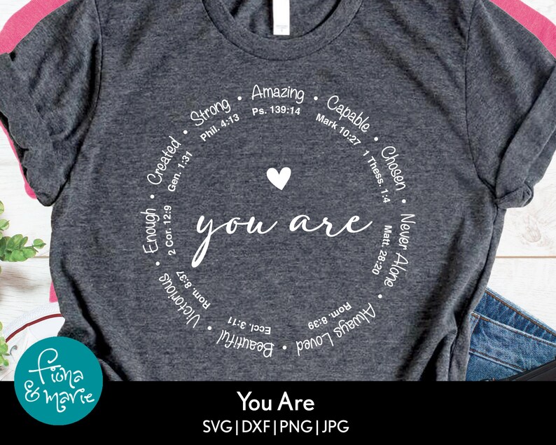 May include: A gray t-shirt with a white circle design that says "you are" with a heart in the center. The circle is surrounded by words and bible verses including "Strong", "Amazing", "Capable", "Chosen", "Never Alone", "Enough", "Created", "Beautiful", "Victorious", "Always Loved".