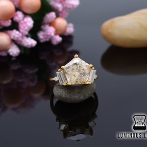 May include: A gold ring with a large, clear, star-shaped gemstone surrounded by smaller, clear gemstones. The ring is resting on a gray stone.