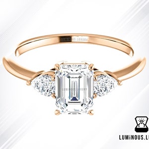 May include: A rose gold engagement ring with a large emerald cut center stone and two pear shaped accent stones.