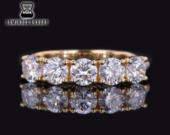 May include: A gold band ring with five round, clear gemstones. The ring is set with a row of five stones, each with a brilliant cut.
