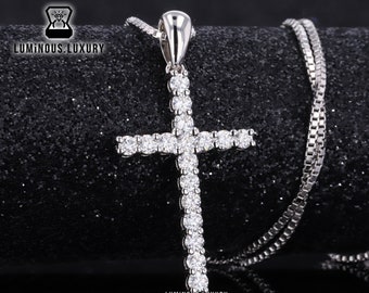 May include: A silver chain necklace with a silver cross pendant encrusted with clear cubic zirconia stones. The pendant is shaped like a traditional cross with a long vertical bar and a shorter horizontal bar. The chain is a delicate box chain.