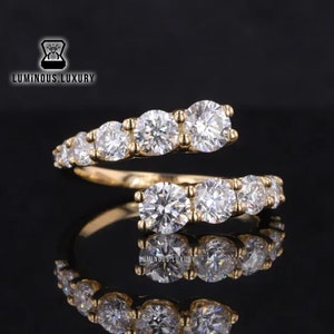 May include: A gold band ring with a row of clear round diamonds on each side. The diamonds are set in a prong setting. The ring is a twist design, with one side of the band wrapping around the other.
