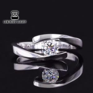 Puede incluir: Un anillo de plata con un solo diamante grande, redondo y transparente engastado en una banda única, curva y retorcida.