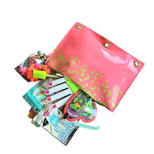 May include: A pink vinyl pouch with green abstract shapes, filled with various items. Contents include a heart-shaped Teenage Mutant Ninja Turtles item, a ruler, a nail art set, and a neon scrunchie. The pouch has three metal grommets.