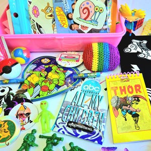 May include: A pink plastic bin filled with various colorful stickers, a rainbow-colored crocheted ball, a Teenage Mutant Ninja Turtles fan, a Thor notepad, and green toy soldiers. Other items include a Pokeball and a Spongebob Squarepants sticker.