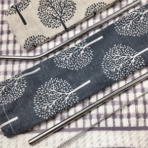 Pode incluir: Conjunto de tr&ecirc;s canudos de beber de a&ccedil;o inoxid&aacute;vel com uma escova de limpeza, em uma bolsa de tecido com padr&atilde;o cinza e branco.