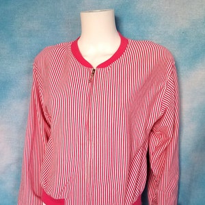 May include: Red and white striped bomber jacket with a full-length zipper. The jacket has a red collar, cuffs, and waistband. The garment is displayed on a white mannequin against a blue background.