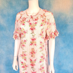 May include: A pink and white floral print short-sleeved dress with a ruffled collar and cuffs. The dress has a button-up front and a knee-length hem.