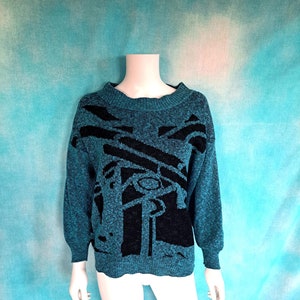 May include: A teal blue sweater with a black abstract design. The sweater has a crew neck and long sleeves.