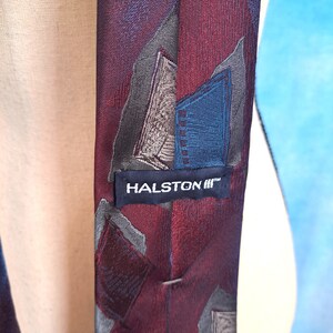 May include: A red, blue, and gray patterned silk tie with a black label that reads "HALSTON III™".