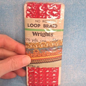 May include: A package of red loop braid by Wrights. The package includes 1 1/2 yards (1.37m) of no iron loop braid. The packaging has a green and tan label with the brand name and product information.