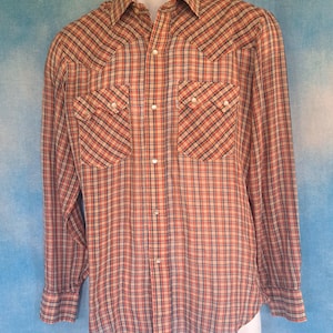 May include: A long-sleeved plaid shirt in shades of red, tan, and navy blue. The shirt features two chest pockets with button closures and pearl snap buttons. The collar and cuffs are also buttoned.
