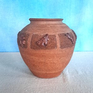 May include: A terracotta vase with a brown glaze and a design of leaves around the middle.
