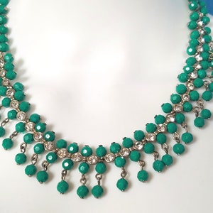 May include: A green and silver beaded necklace with a cascading design. The necklace features small, round green beads and clear rhinestones.