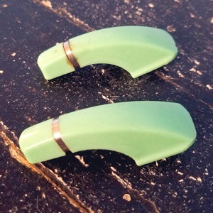 May include: Two vintage green plastic pot handles with silver metal bands. The handles are curved and have a smooth, glossy finish.
