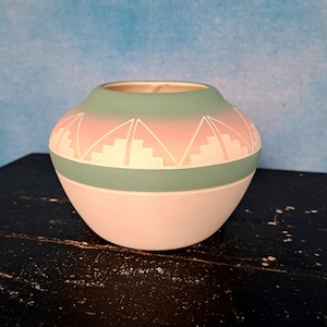 May include: A white ceramic pot with a light green and pink geometric design. The pot has a rounded shape and a wide opening.