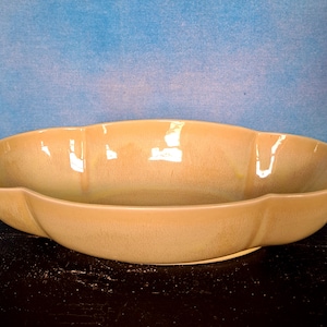 May include: A large, oval-shaped, yellow ceramic bowl with a slightly rippled surface. The bowl has a unique, organic shape with a slight curve on each side.