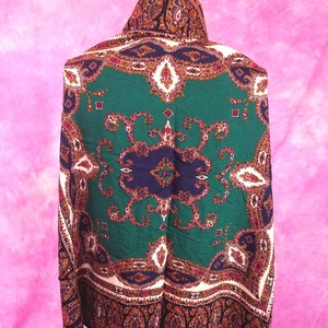 May include: A green, blue, and brown paisley patterned scarf with a white border. The scarf is draped over a black mannequin.