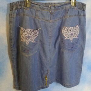 May include: A blue denim skirt with a stretchy waistband and embroidered floral details on the back pockets.