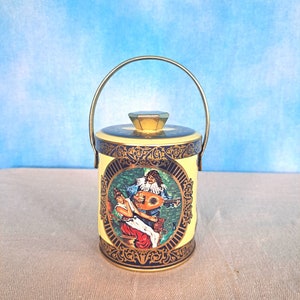 May include: A yellow and blue metal tin with a gold handle. The tin has a decorative design featuring a couple playing music.