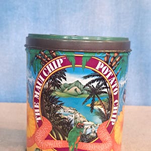 May include: A cylindrical tin featuring a tropical scene with palm trees, ocean waves, and a parrot. The words "The Maui Chip Potato Chip" are displayed around the central image. The tin has a green lid and the text "No-Ka-Oi" at the bottom.
