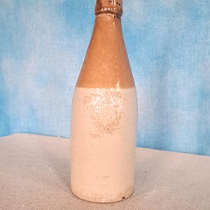 May include: A brown and white ceramic bottle with a rounded bottom and a narrow neck. The bottle is glazed and has a rustic appearance.