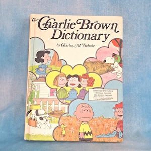 May include: A vintage copy of "The Charlie Brown Dictionary" by Charles M. Schulz. The cover features colorful illustrations of Peanuts characters like Charlie Brown, Snoopy, and Lucy. The book is in full color and defines 2400 words.