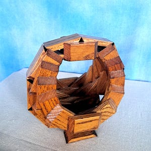 May include: A handcrafted wooden puzzle in a geometric shape. The puzzle is constructed from various shades of brown wood, creating a visually appealing contrast. The design features an open center and a sturdy base.