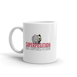 May include: White ceramic mug featuring a black and grey cat illustration. The text "SUPERPOSITION NOT SUPERSTITION" is printed in red on the mug.