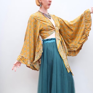 May include: A mustard yellow wrap top featuring a small floral pattern, wide bell sleeves with ruffled edges, and a front tie closure. The top is paired with a solid teal green maxi skirt that has a gathered elastic waistband and a flowing silhouette.